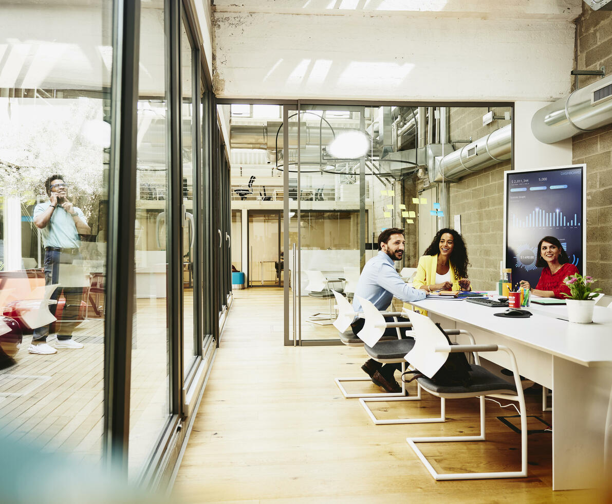 Three colleagues having a meeting in a meeting room, while one colleague is making a call outside the room.
